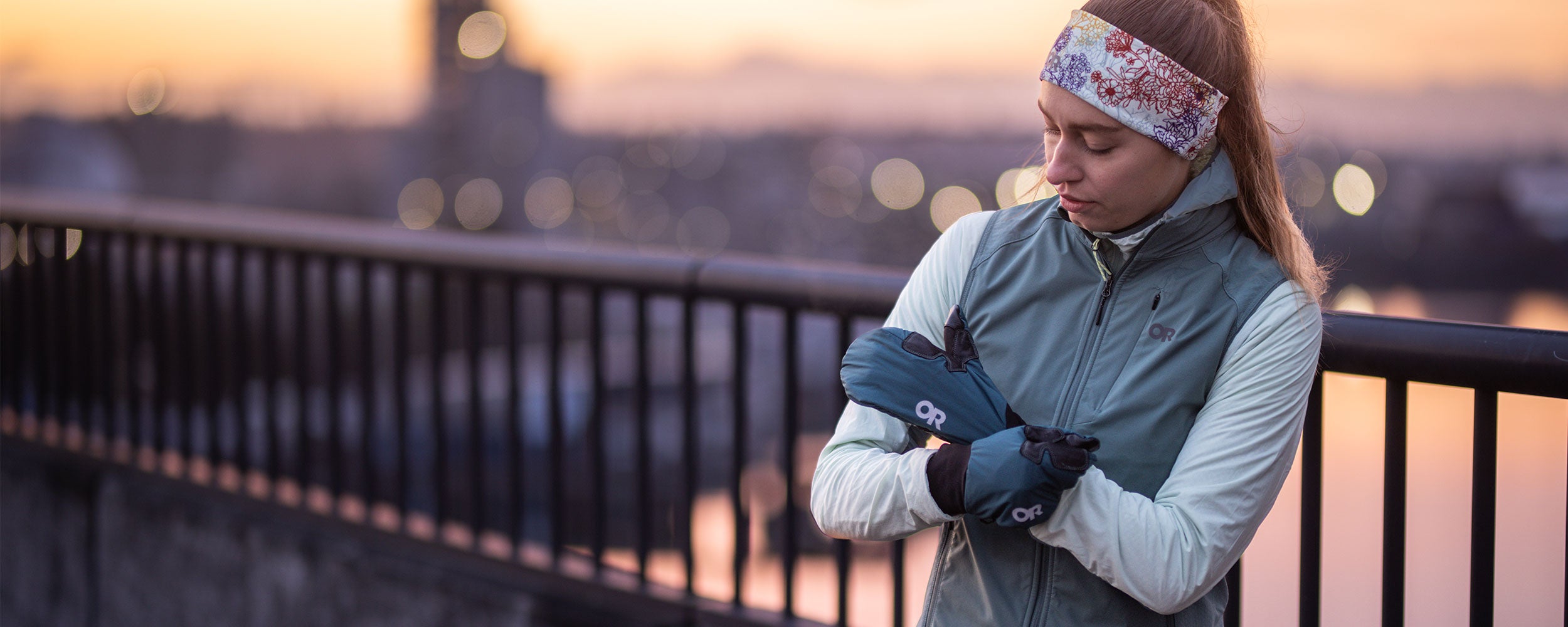 A woman wearing the Outdoor Research Deviator Sportswear collection tightens her Deviator Mitts in Harbor blue before a run. 