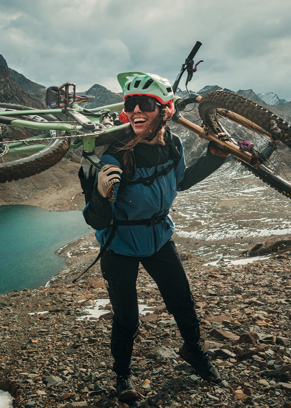 Female holding her bike on her back wearing Outdoor Research Women's Freewheel MTB Stretch Rain Jacket Galactic/Black and Freewheel MTB Leather Palm Bike Gloves Khaki. 
