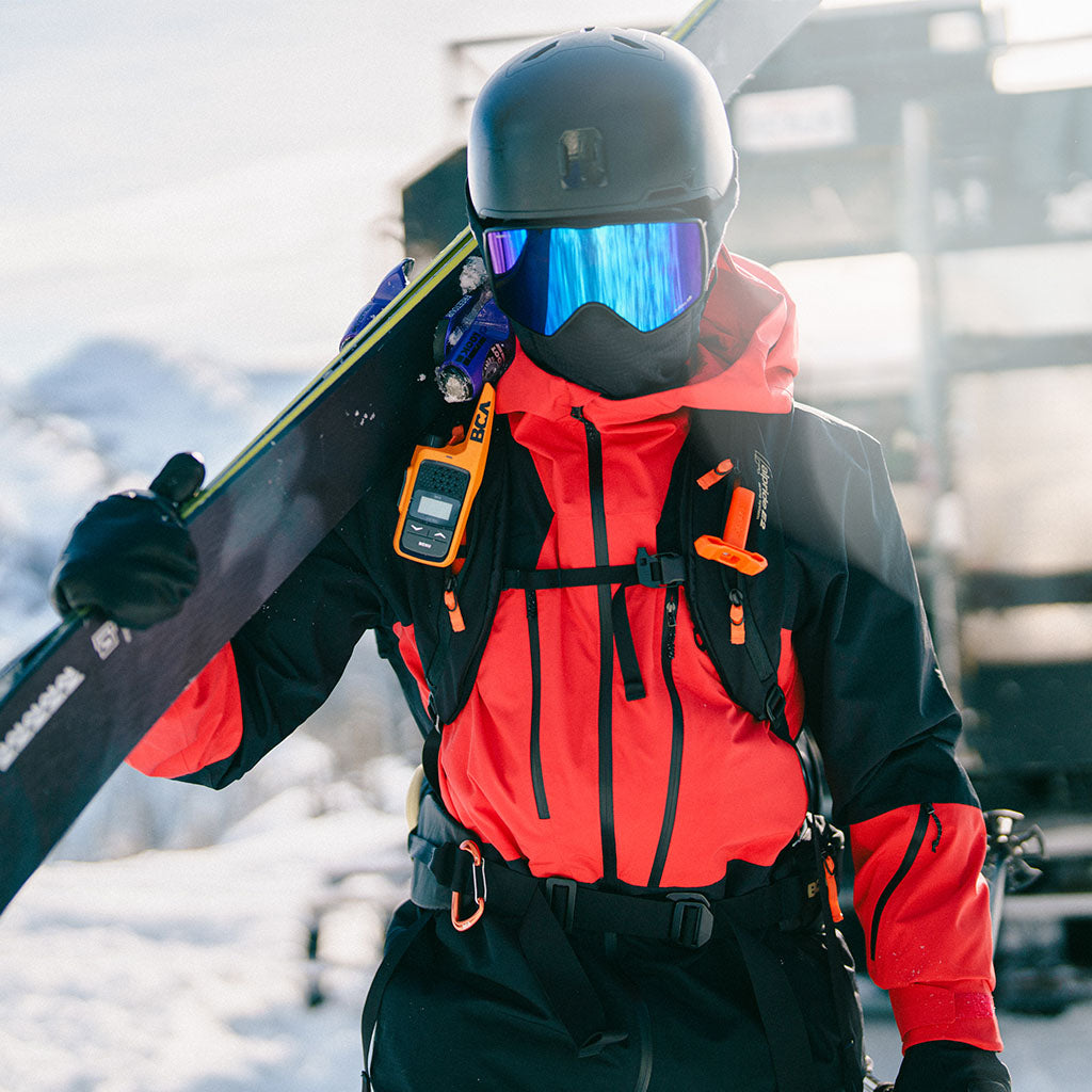 Male holding his skis on his shoulder wearing Outdoor Research Men's Powderverse Jacket Lingonberry/Black. 